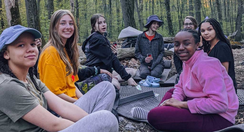 a group of girls sit at a campsite on a course with outward bound